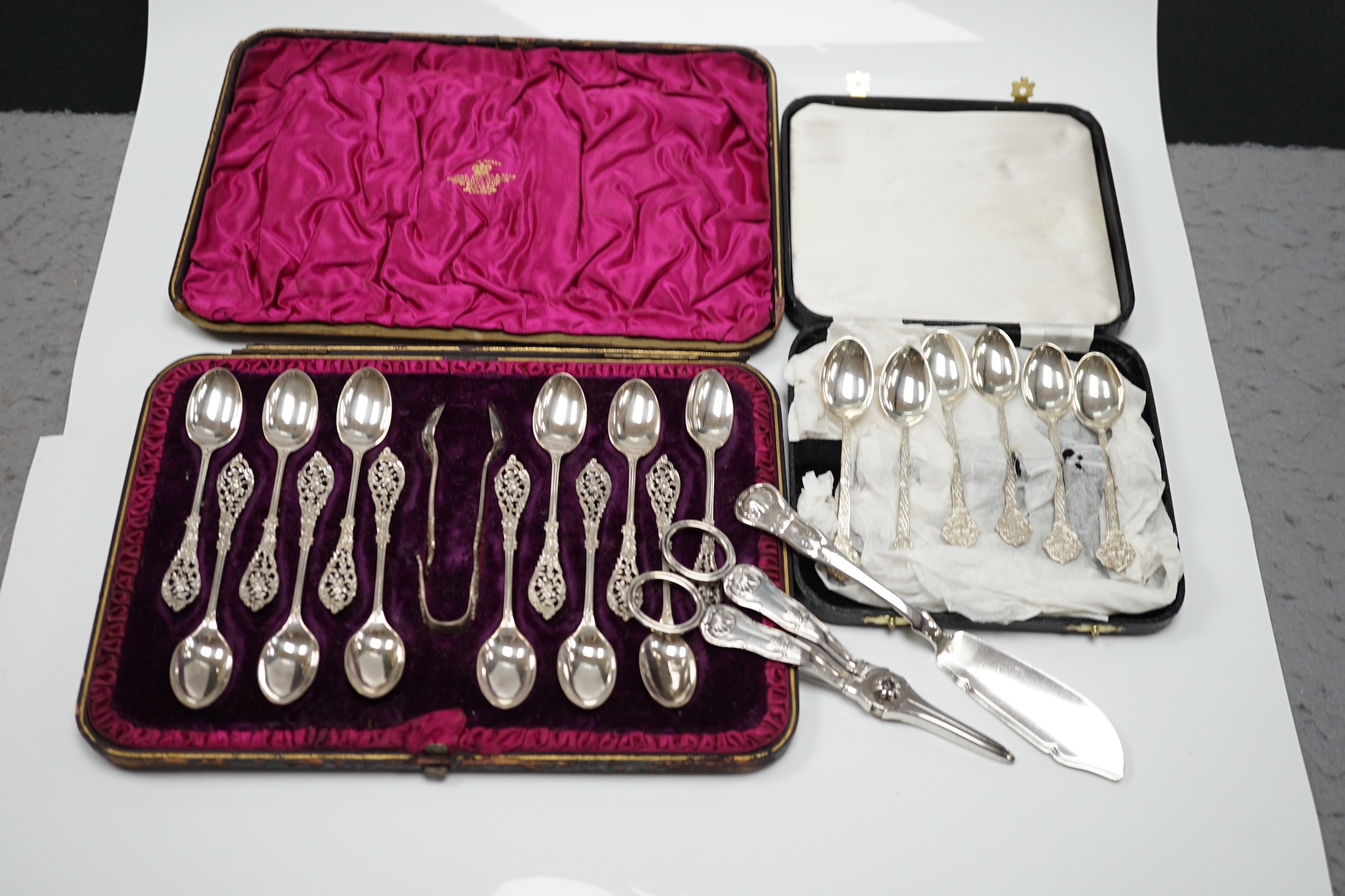A cased set of twelve Victorian silver teaspoons, with pierced terminals by William Comyns, London 1889, with a damaged pair of matching sugar tongs, a cased set of six later teaspoons, a pair of George IV silver King's